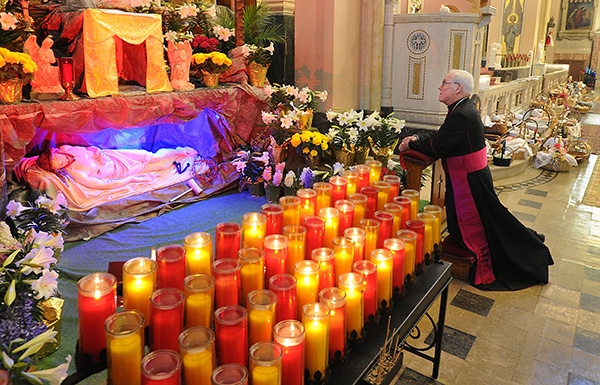 Framed by prayer candles and Easter Baskets waiting to be Blessed Bishop Richard J. Malone prays at the Tomb of Jesus in the Sacristy at Corpus Christi Church before blessing the baskets. (Dan Cappellazzo/Staff Photographer)